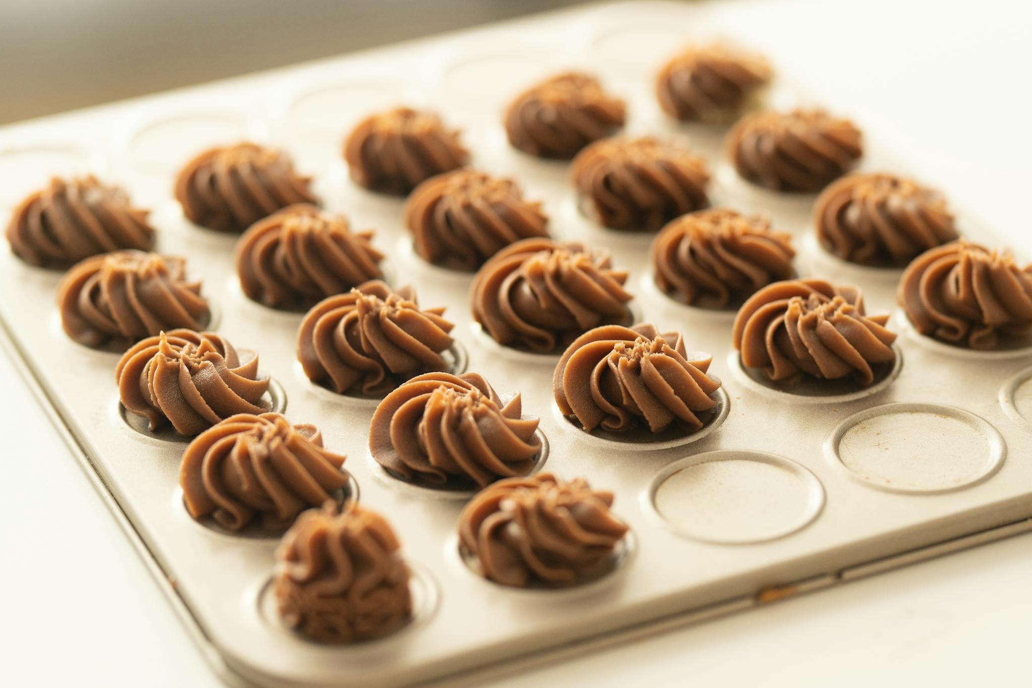 Close-up of chocolate frosted pastries arranged neatly on a baking tray, ready to bake.