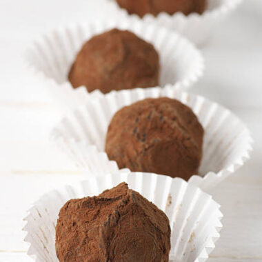 Homemade chocolate truffles with cocoa powder in white paper cups.